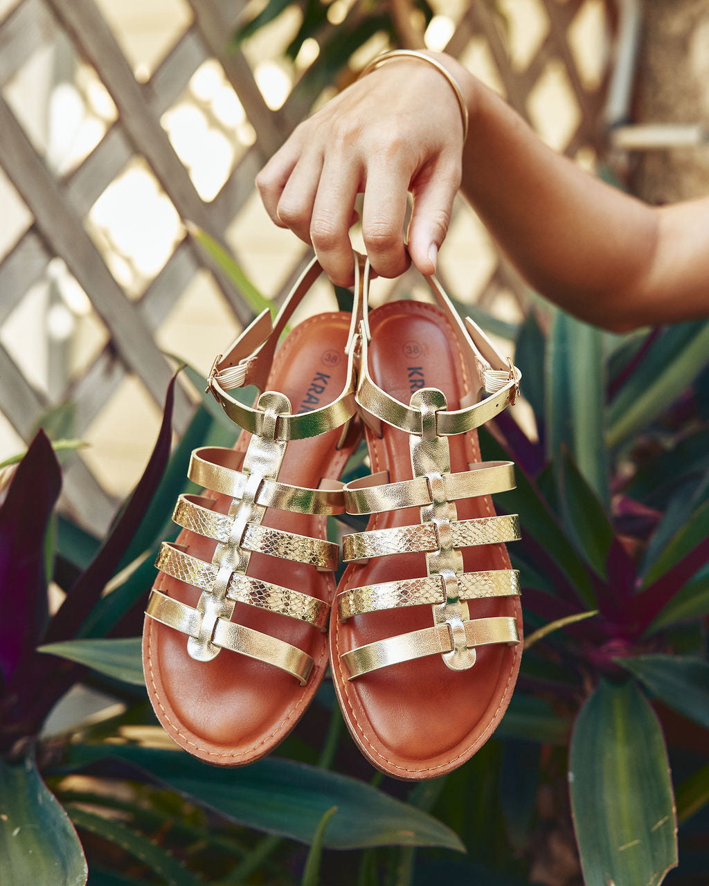Sandales femme dorées tenues à la main dans un décor tropical — collection sandales Influence La Réunion